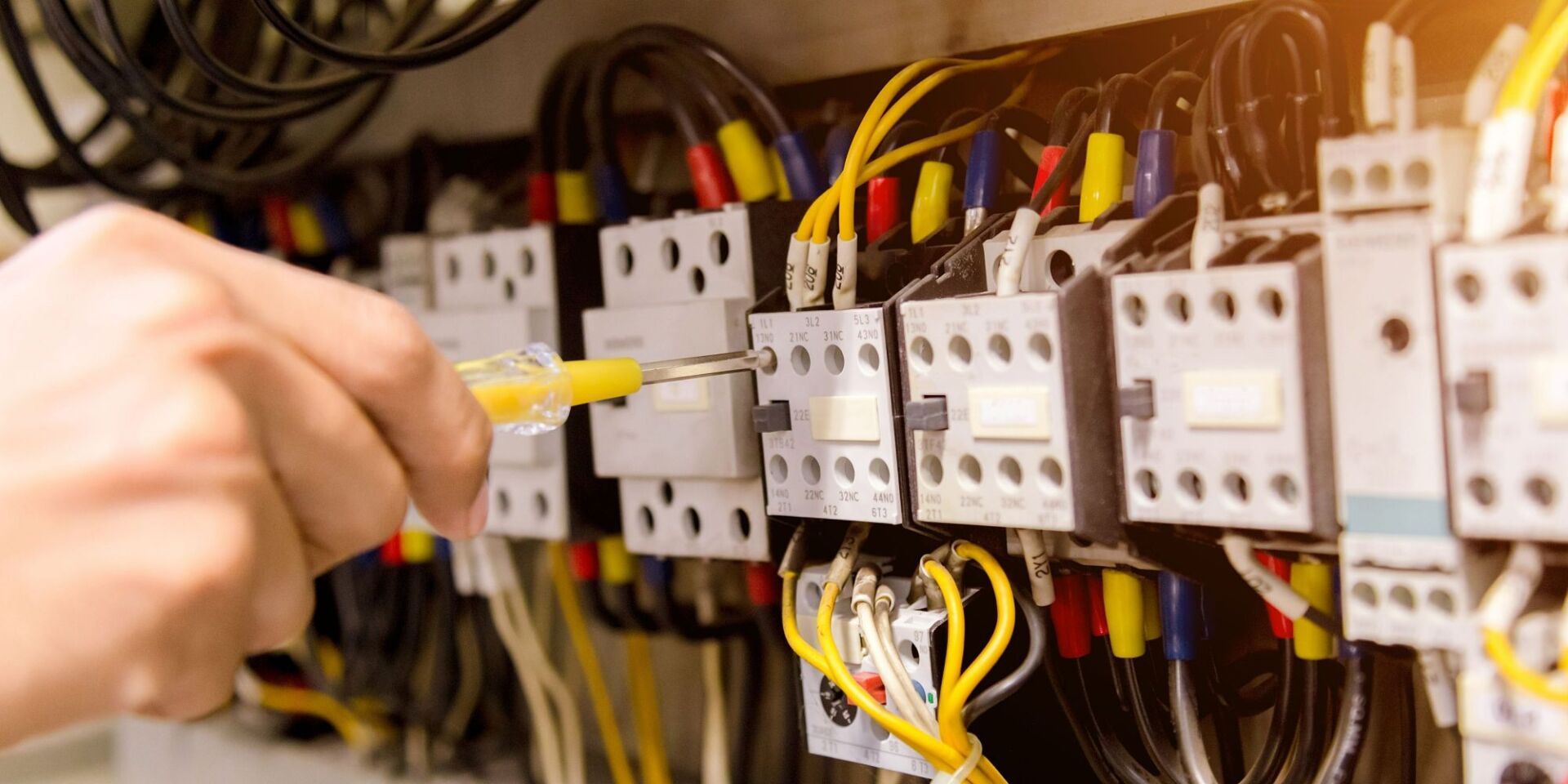 A person using a yellow screwdriver to work on electrical wiring in a panel.