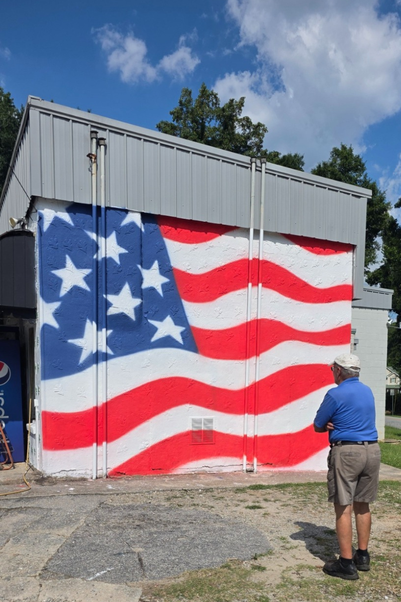 A man stands in front of an american flag painted on the side of a building