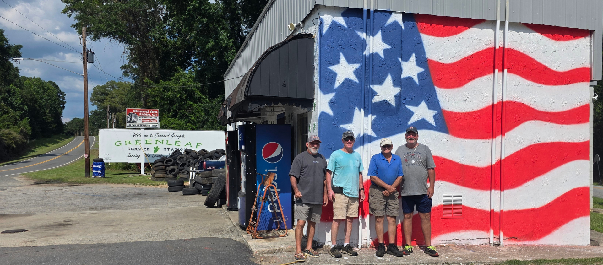 A group of men are standing in front of an american flag painted on the side of a building.
