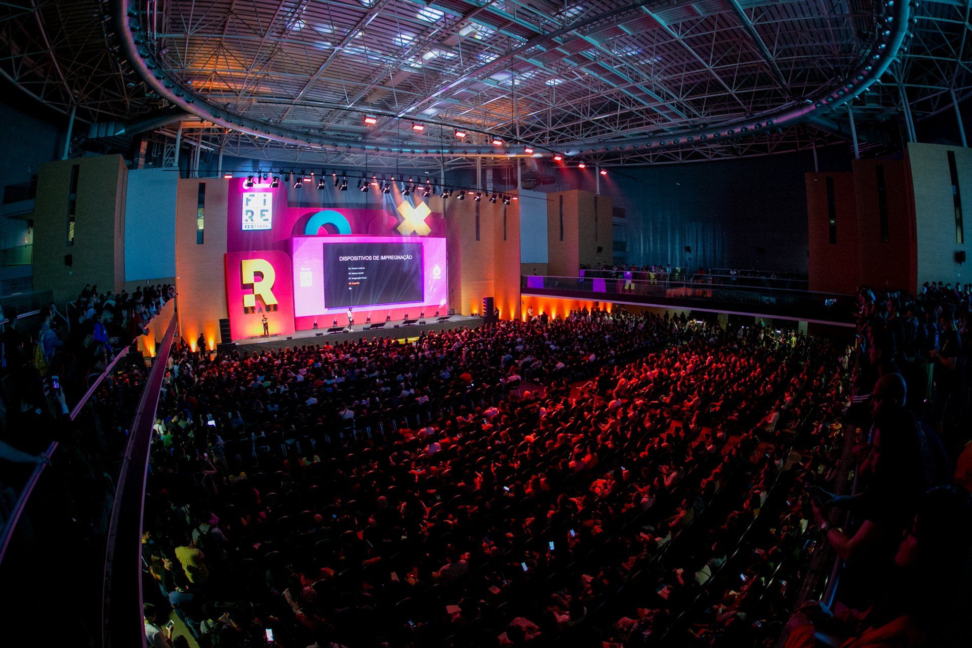 Uma grande multidão de pessoas está sentada em frente ao palco em um show.