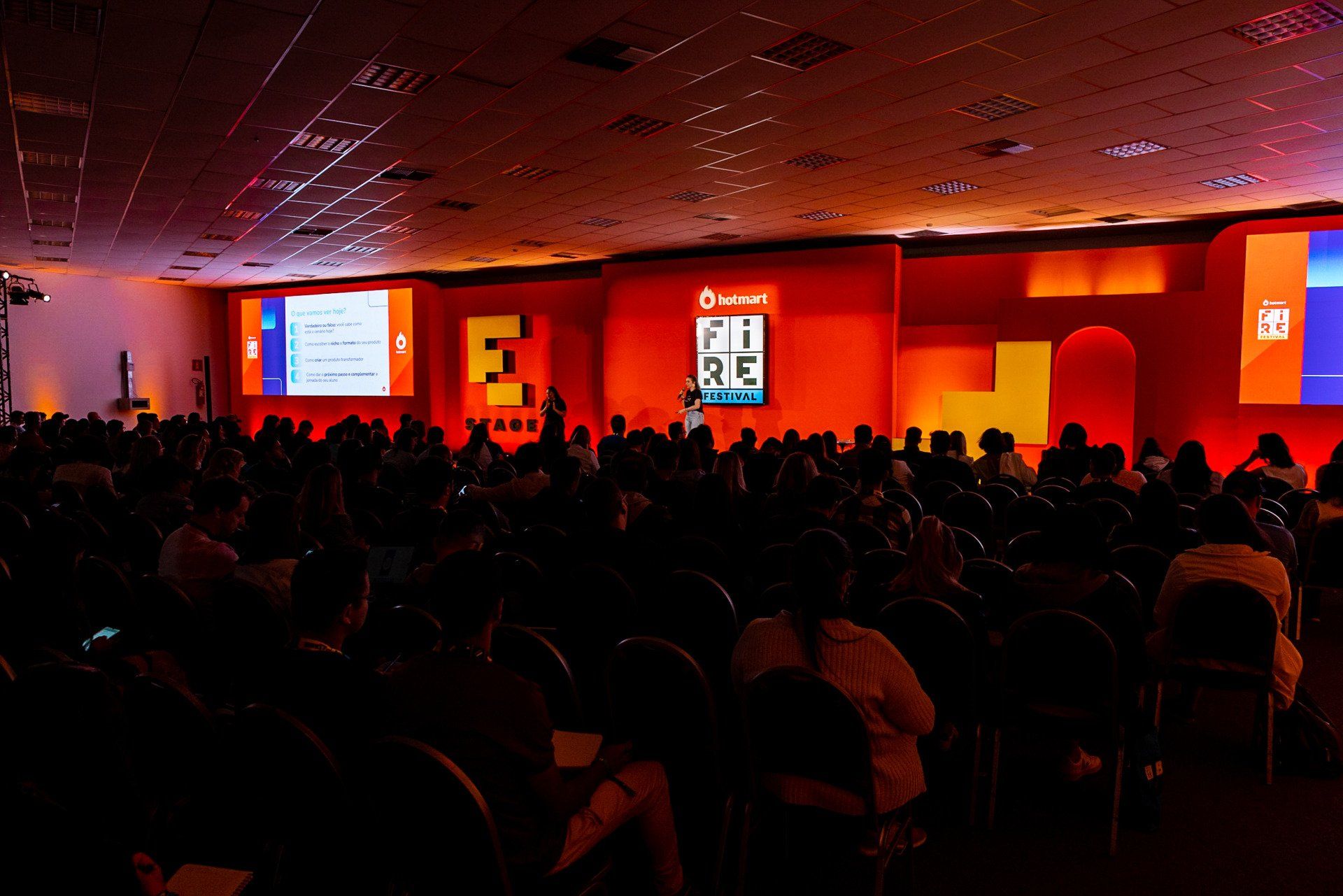 Um grande grupo de pessoas está sentado em um auditório escuro assistindo a uma apresentação.