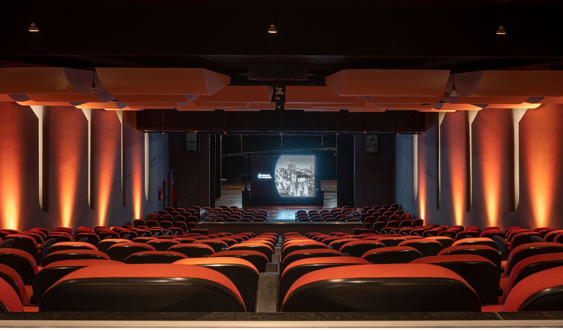 Un gran auditorio lleno de asientos rojos y una pantalla de proyección.