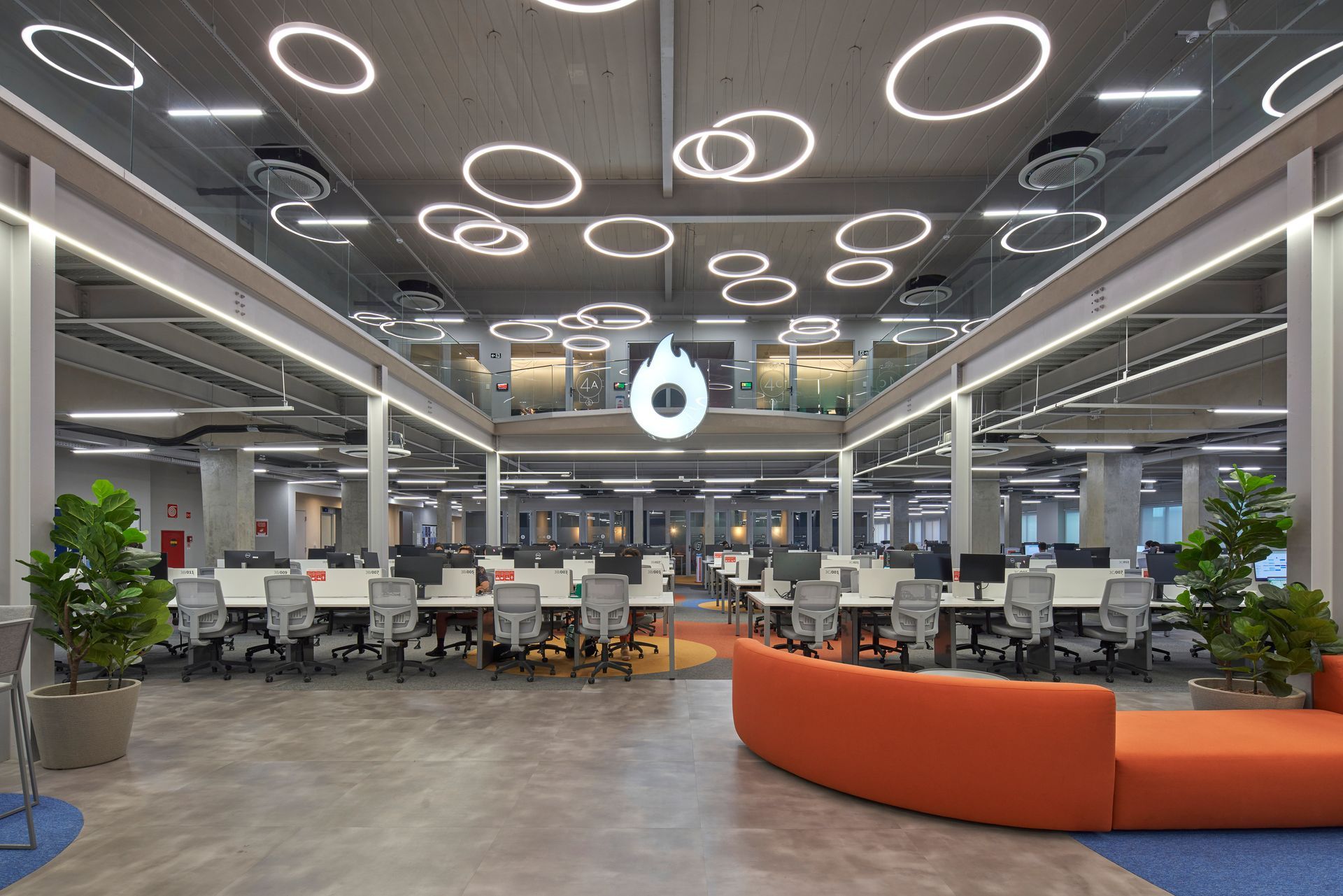 Una oficina grande con muchas mesas y sillas y un gran sofá naranja.