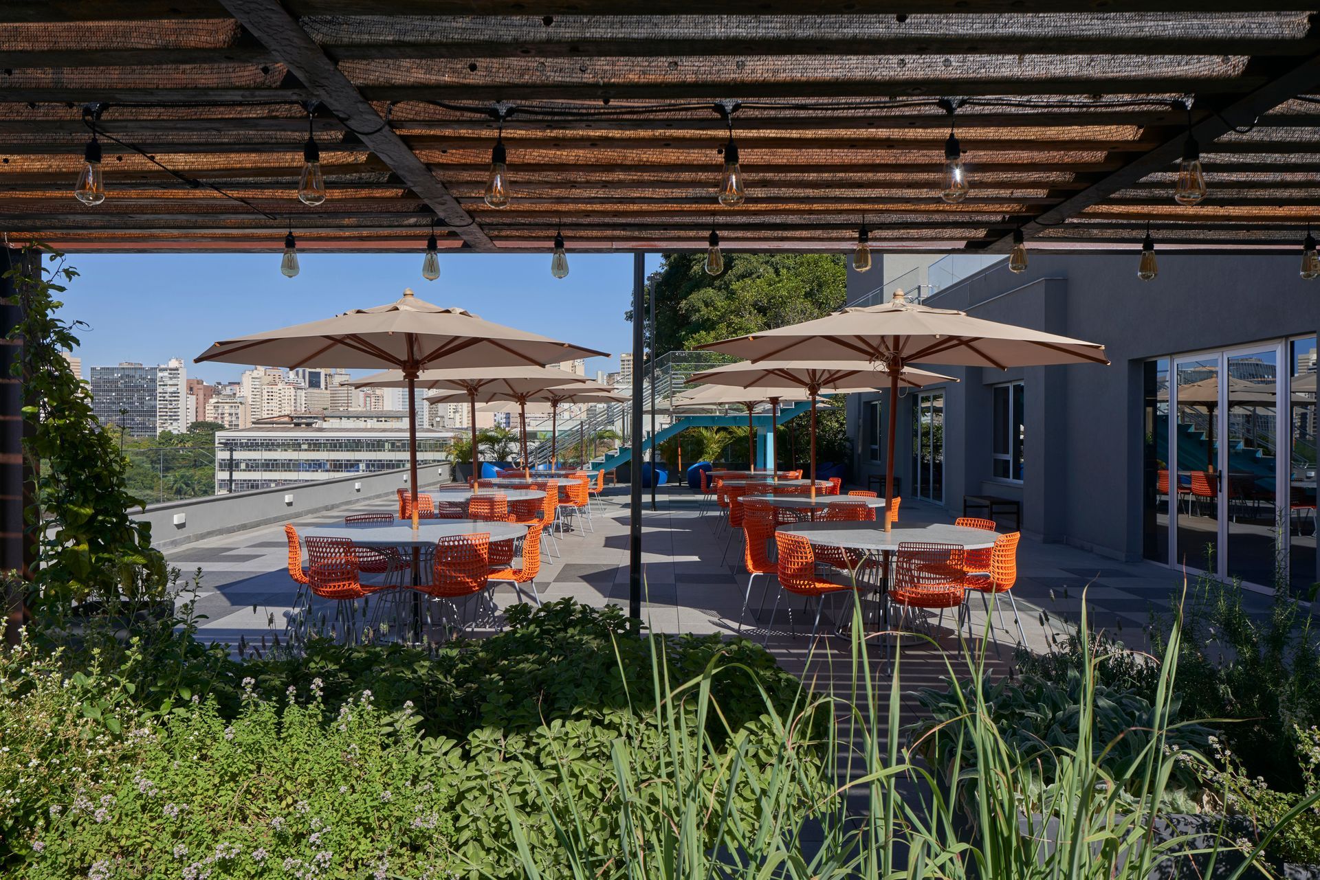 Un patio con mesas y sillas y sombrillas bajo una pérgola.