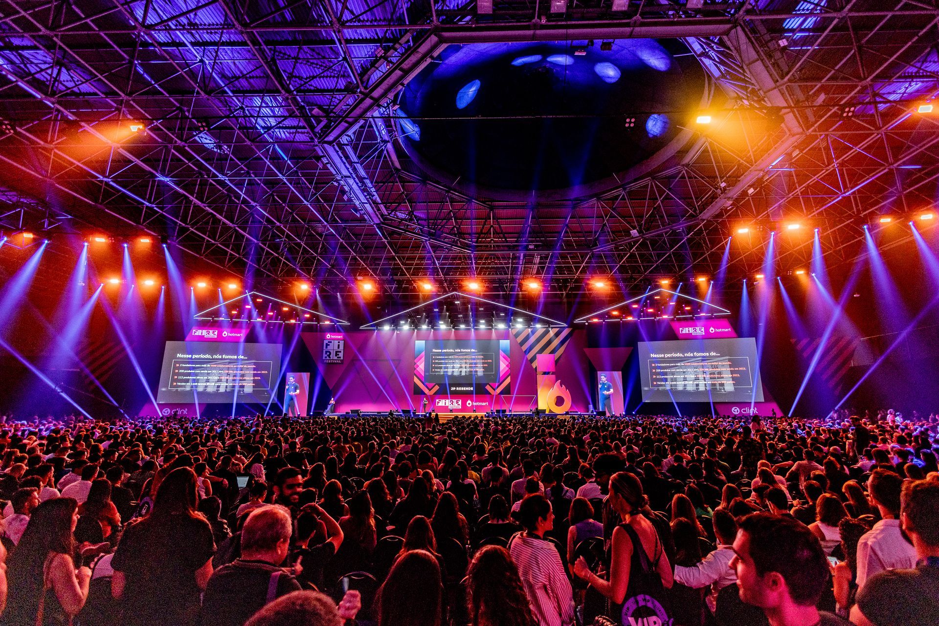 Uma grande multidão de pessoas está sentada em frente ao palco em um show.