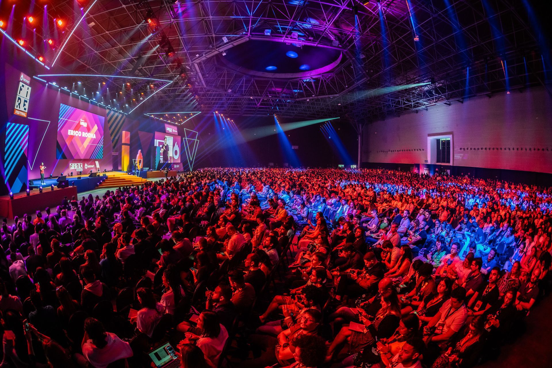 Uma grande multidão de pessoas está sentada em frente ao palco em um show.