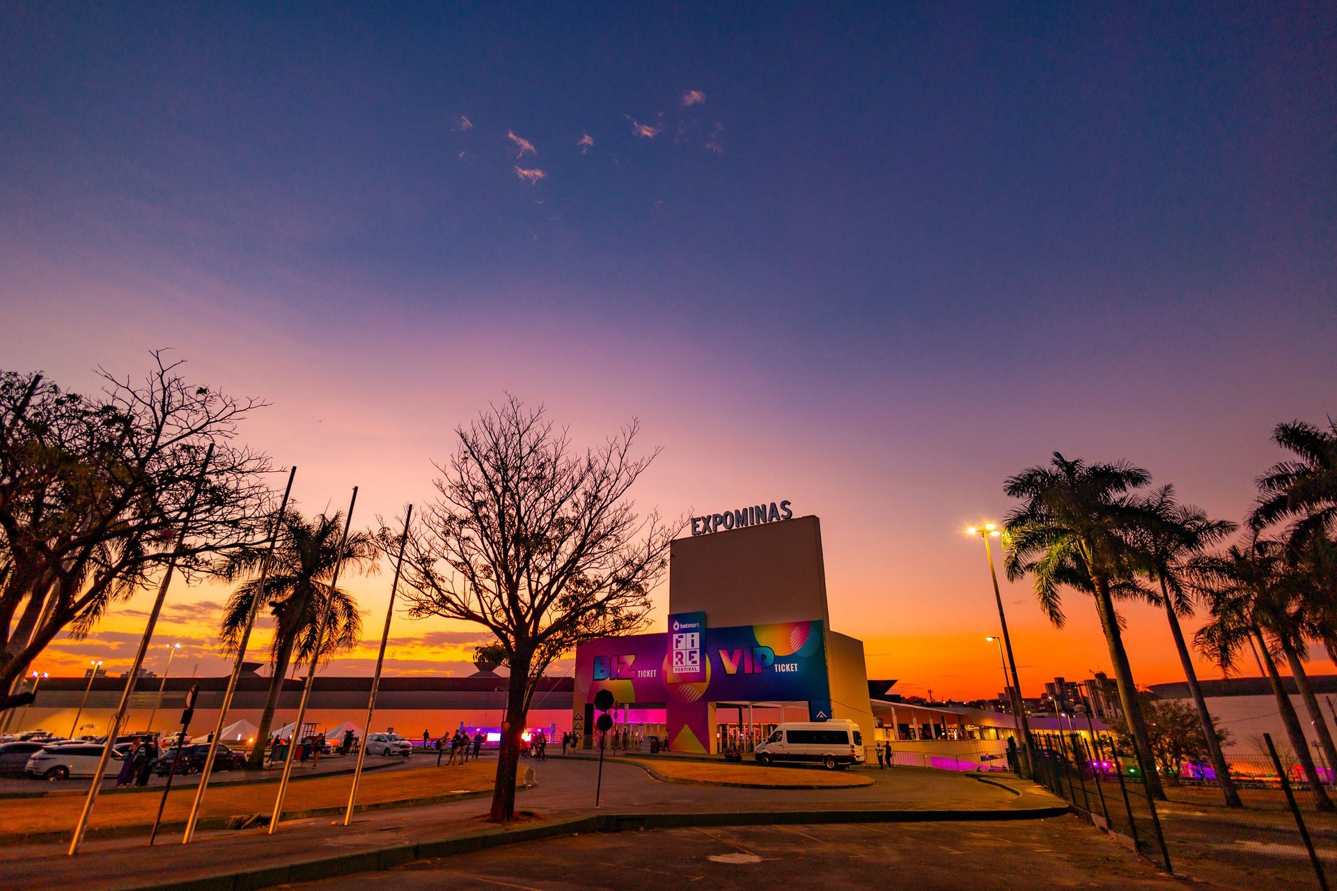 Um pôr do sol sobre um estacionamento com palmeiras e um prédio ao fundo.