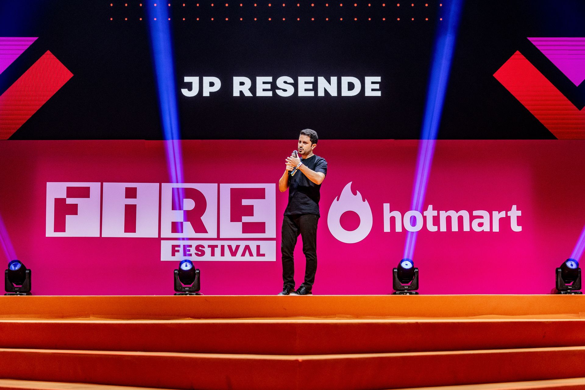 Um homem está em pé em um palco em frente a uma placa que diz festival do fogo