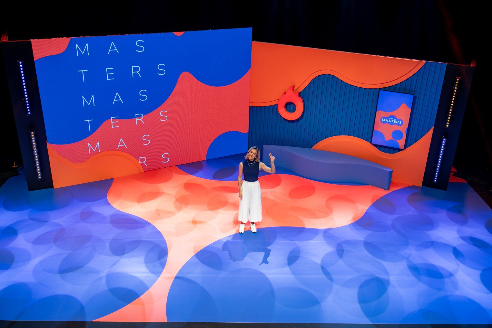 Uma mulher está de pé no palco em frente a uma tela grande.