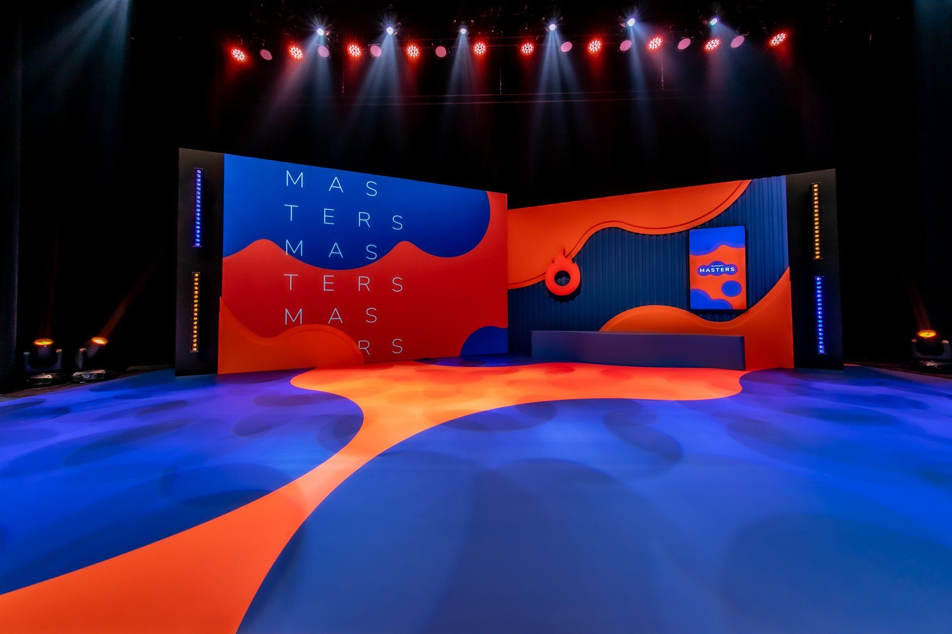 Um palco com um tapete azul e laranja e uma tela grande atrás dele.