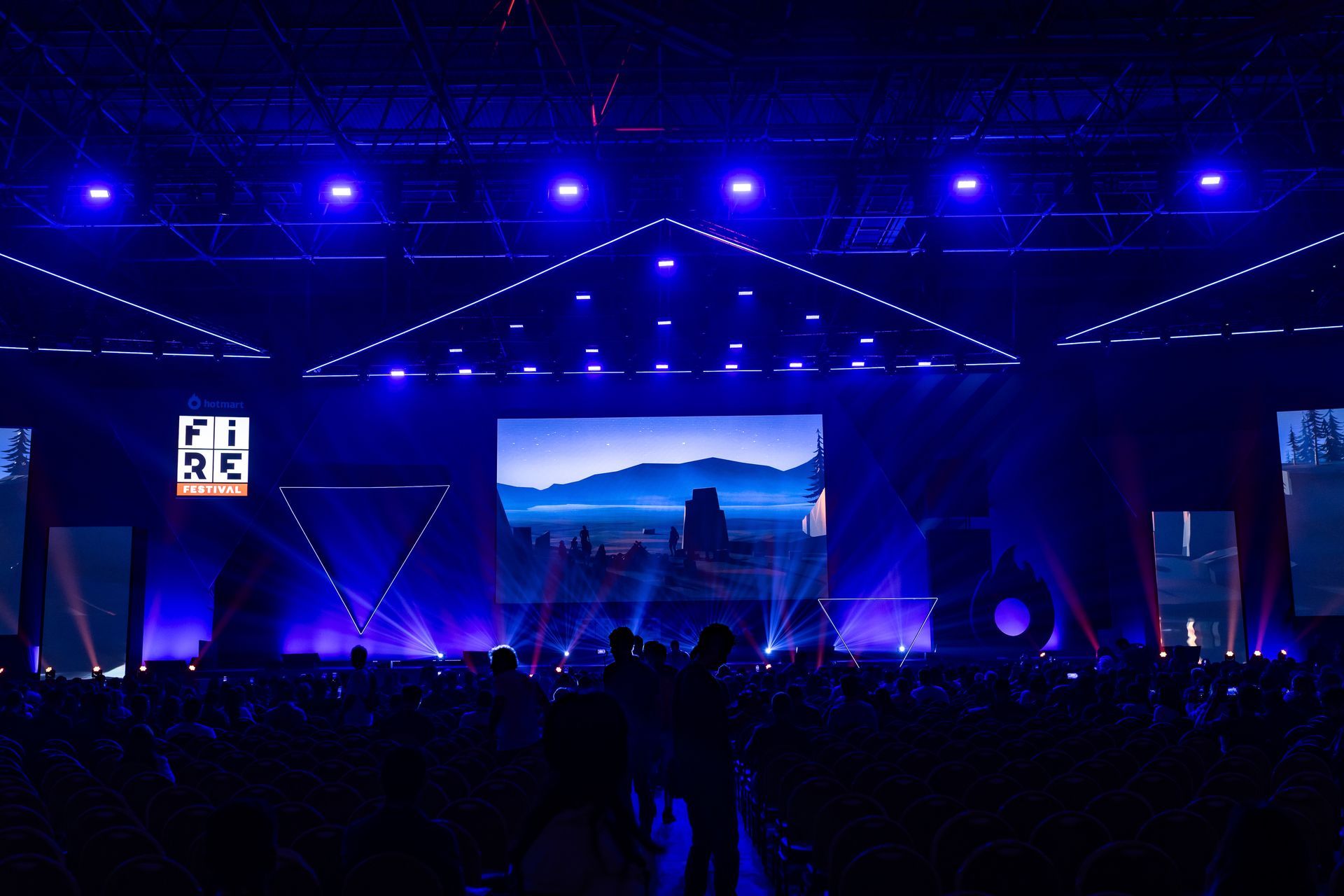 Uma multidão de pessoas se reúne em frente a um palco com uma tela grande que diz re