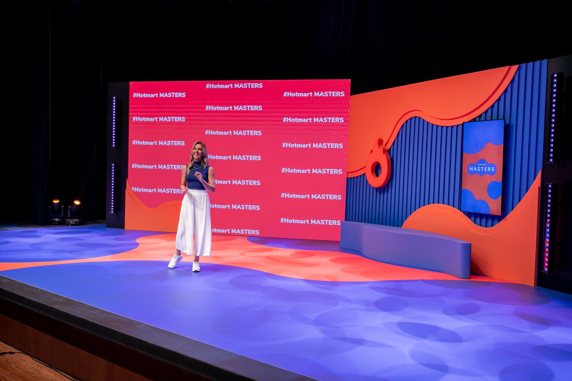 Uma mulher está de pé no palco em frente a uma tela grande.
