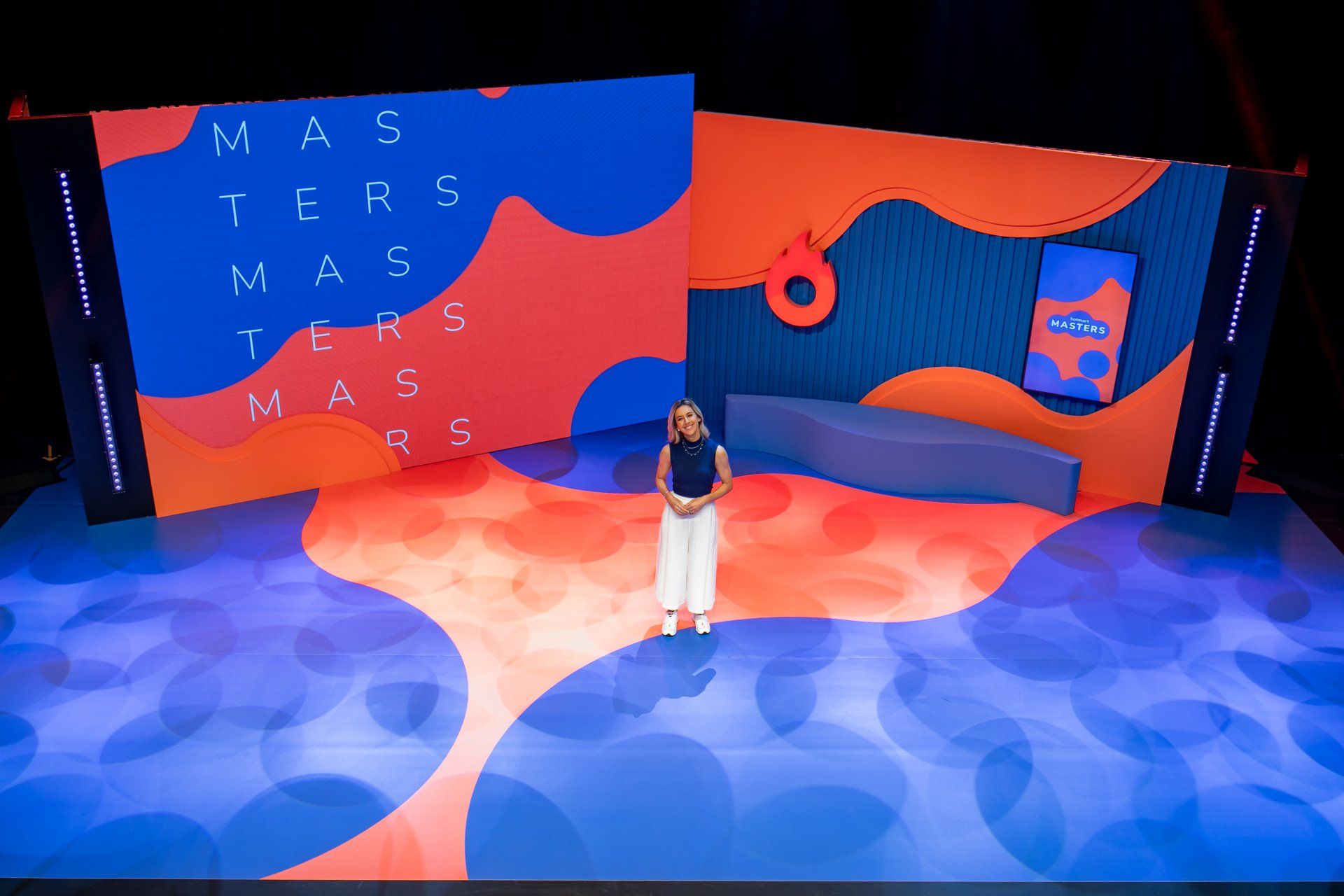 Uma mulher está de pé no palco em frente a uma tela grande.