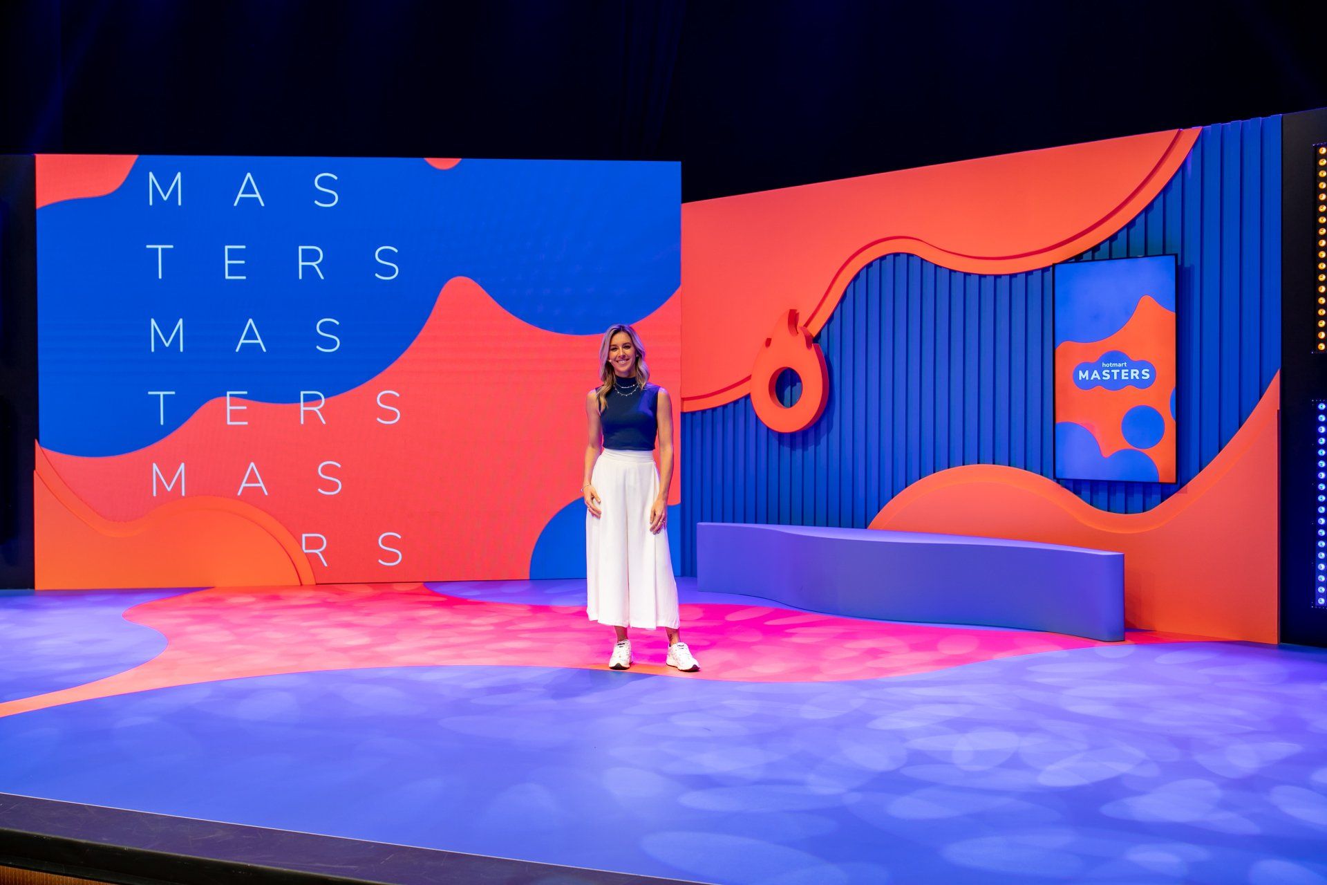 Uma mulher está de pé no palco em frente a uma tela grande.