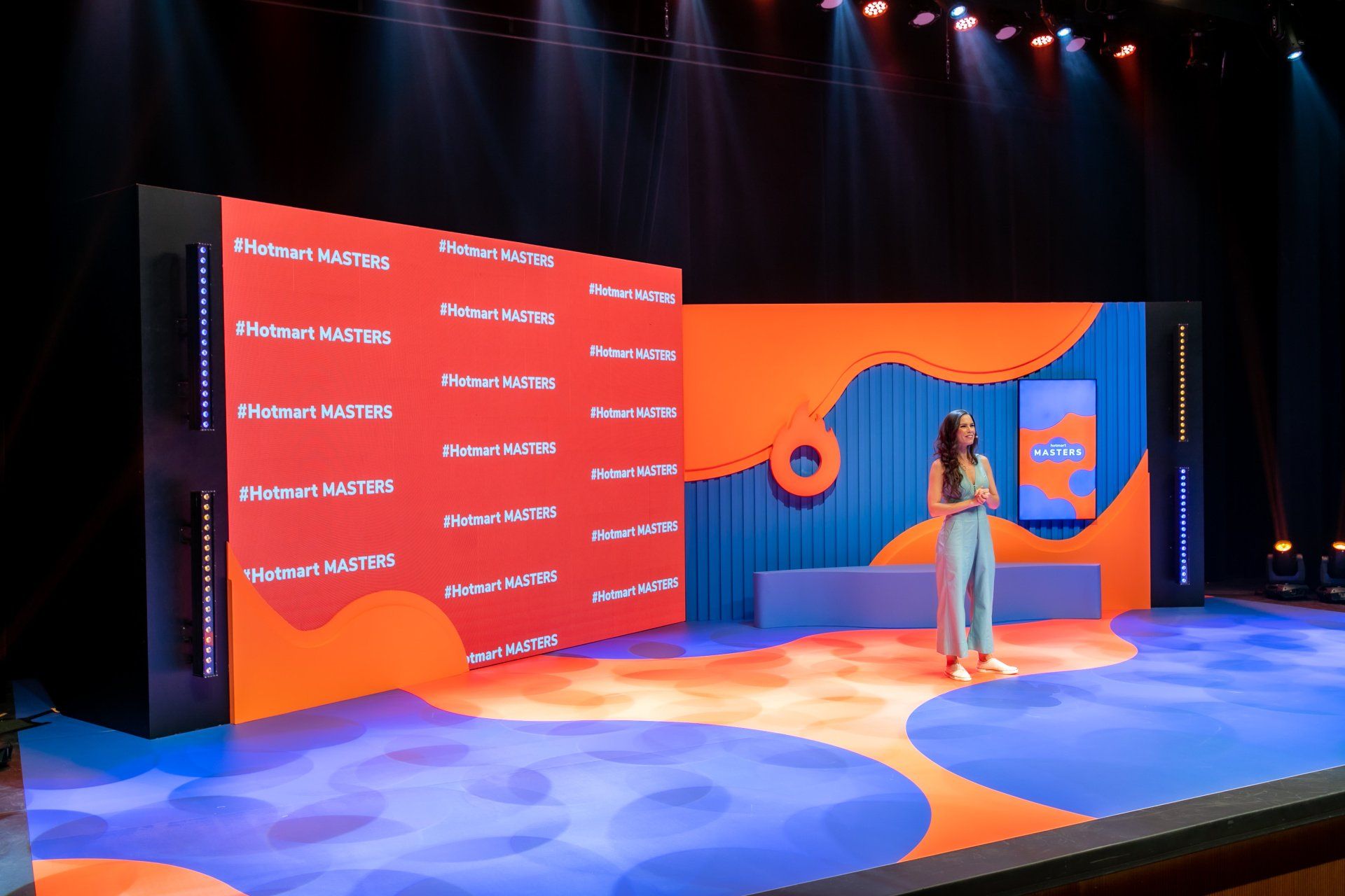 Uma mulher está de pé no palco em frente a uma tela grande.