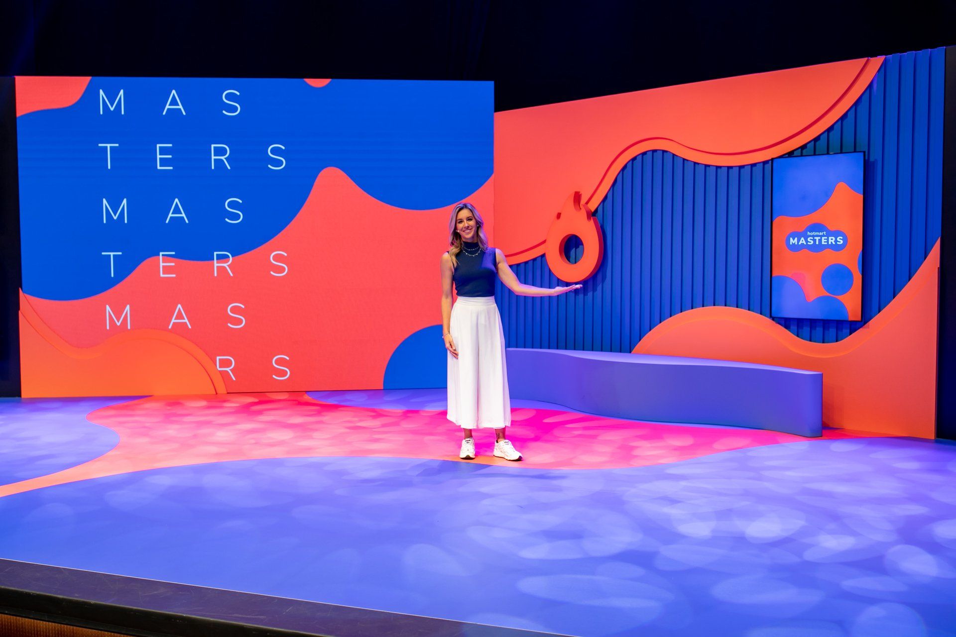 Uma mulher está de pé no palco em frente a uma tela grande.