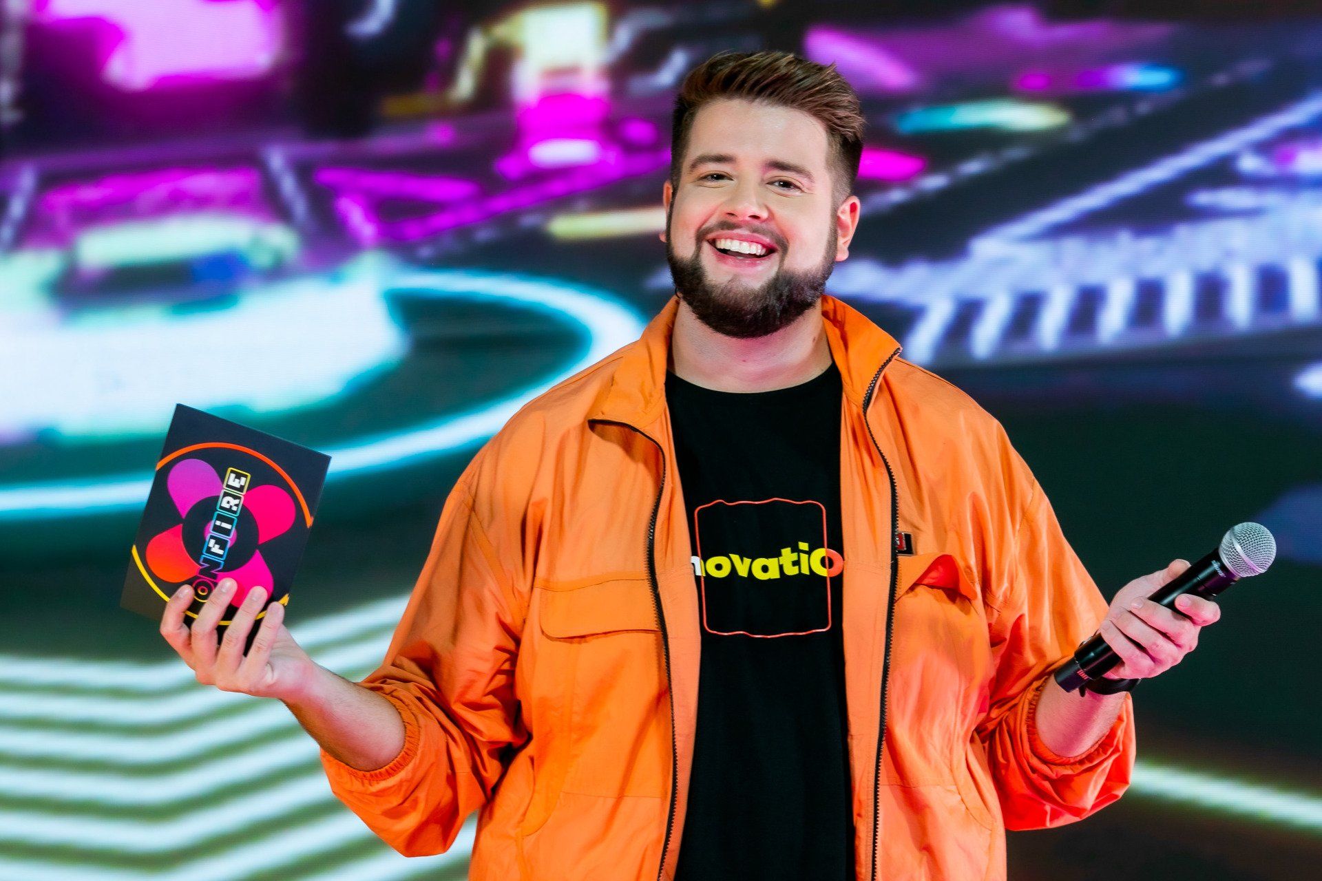 Um homem de jaqueta laranja está segurando um microfone e um CD.