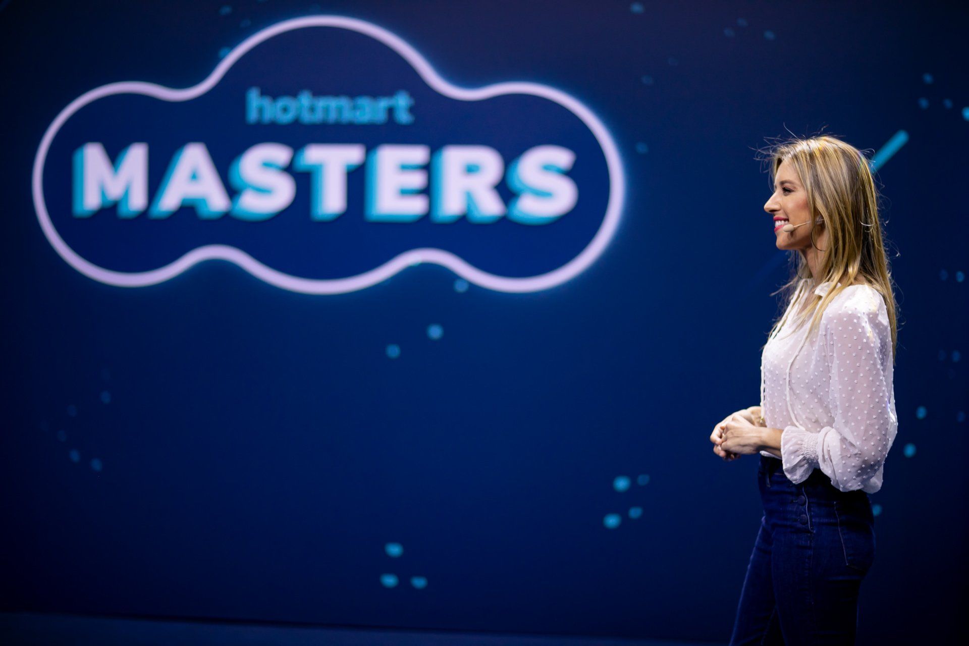 Uma mulher está parada em frente a uma placa que diz hotmart masters.