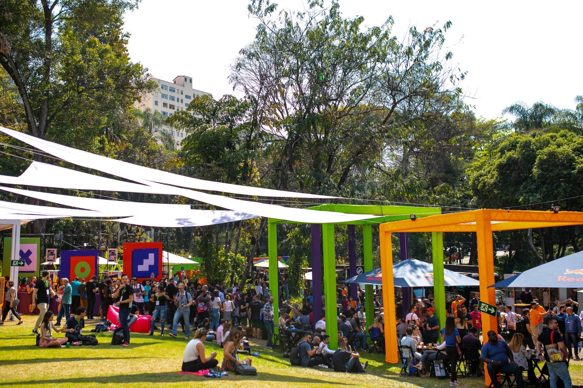 Um grande grupo de pessoas está sentado sob guarda-sóis em um parque.