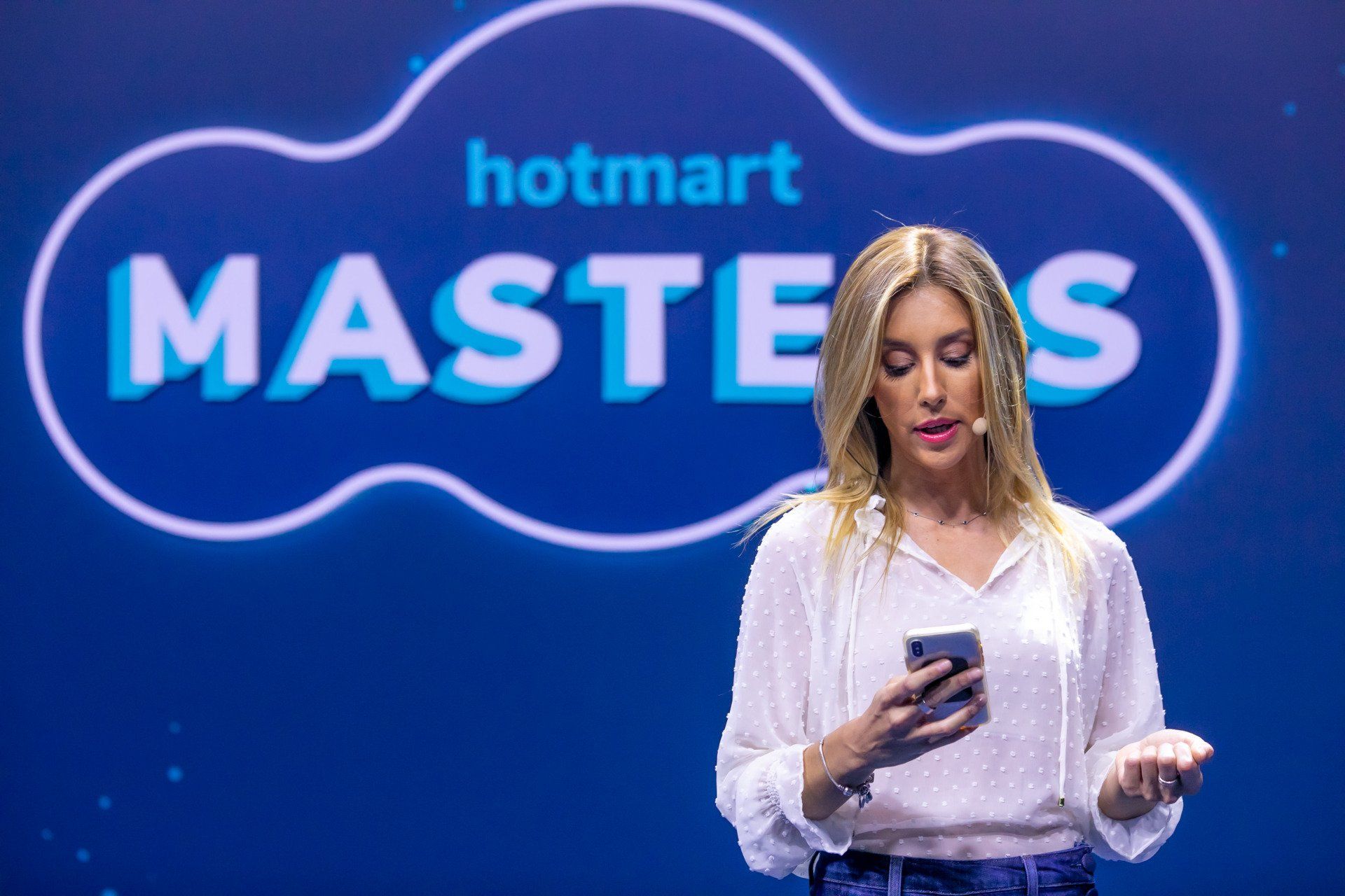 Uma mulher está parada em frente a uma placa que diz hotmart masters