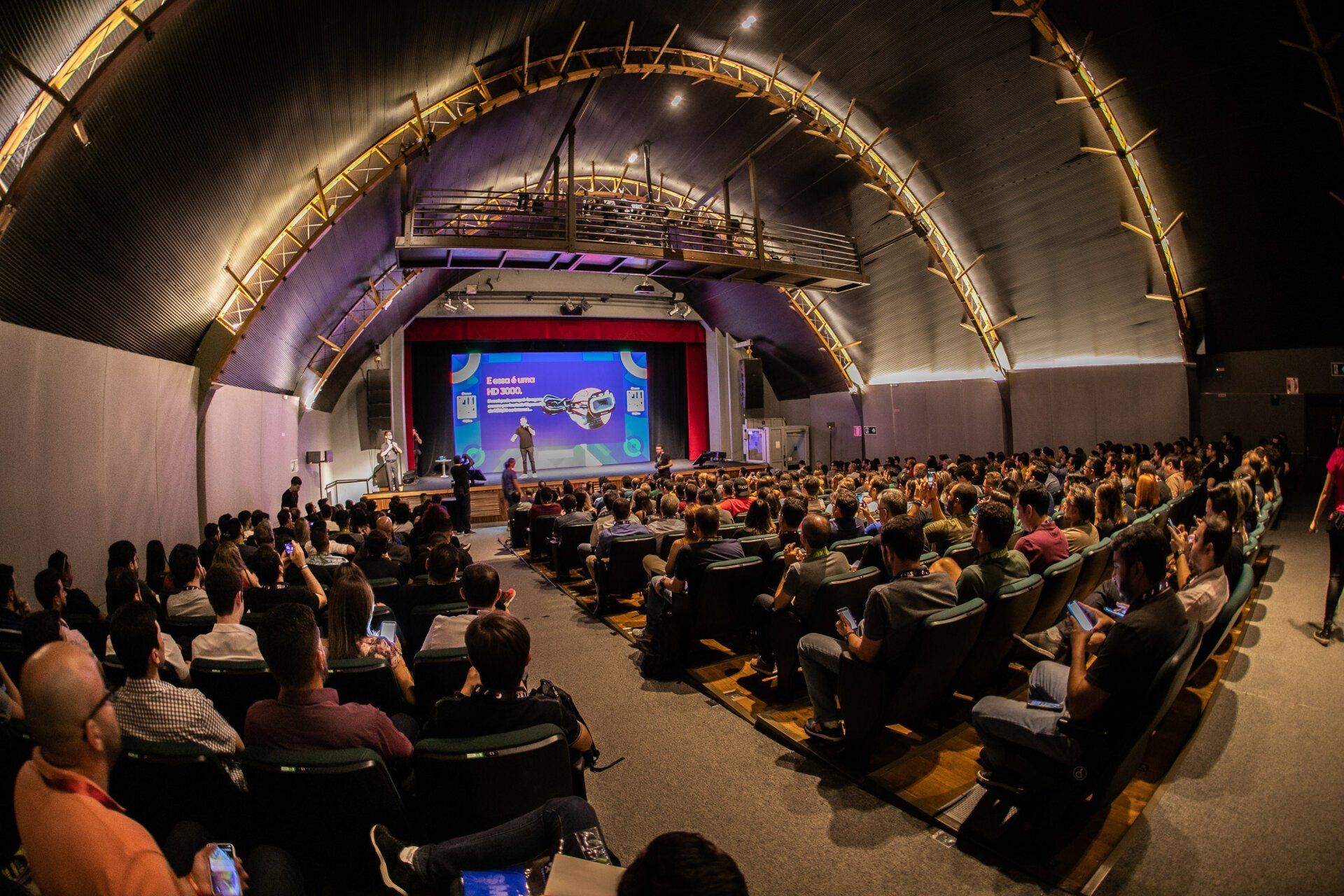 Um grande grupo de pessoas está sentado em um auditório assistindo a uma apresentação.