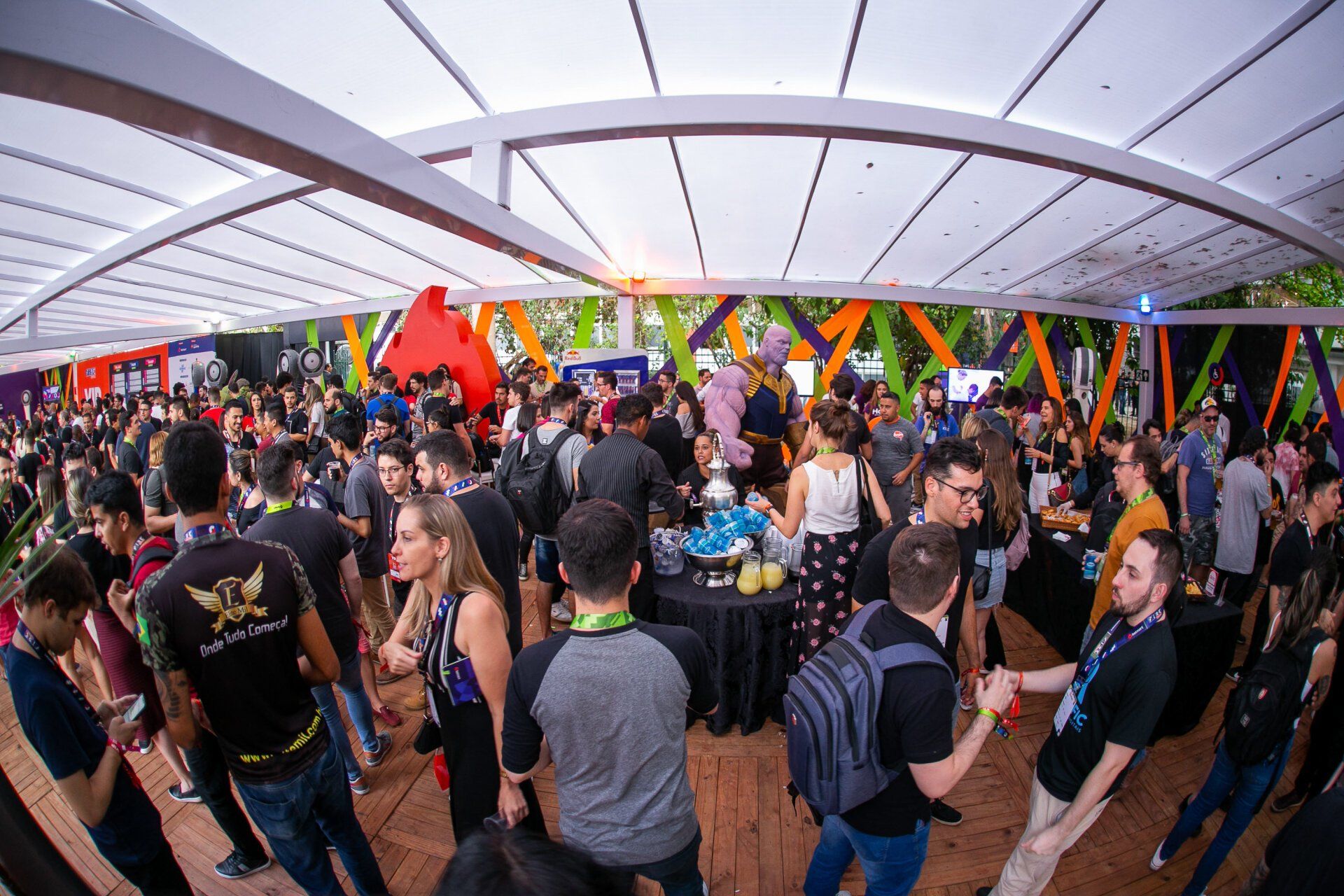 Um grande grupo de pessoas está em uma sala sob uma tenda.