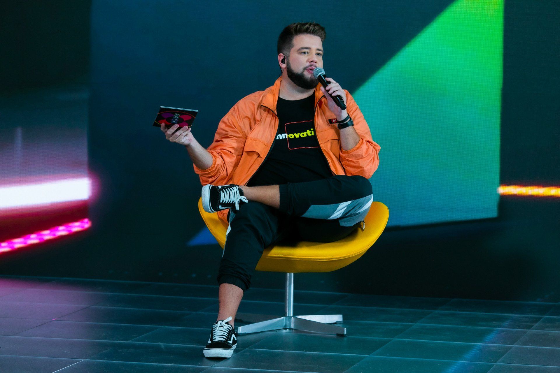 Um homem está sentado em uma cadeira amarela segurando um microfone.