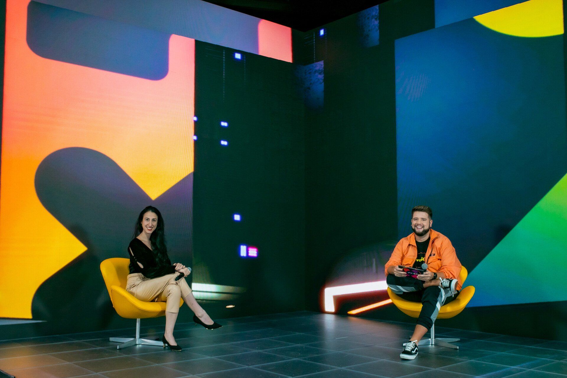 Um homem e uma mulher estão sentados em cadeiras em frente a uma tela grande.