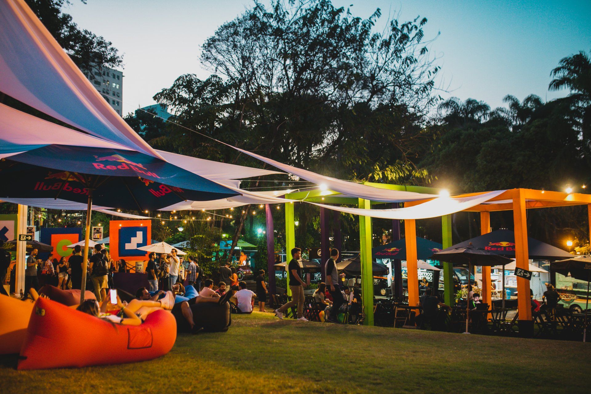 Um grupo de pessoas está sentado sob guarda-sóis em um parque.