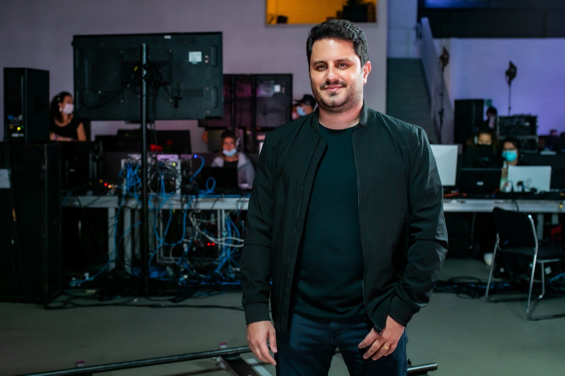 Um homem de jaqueta preta está parado em uma sala.