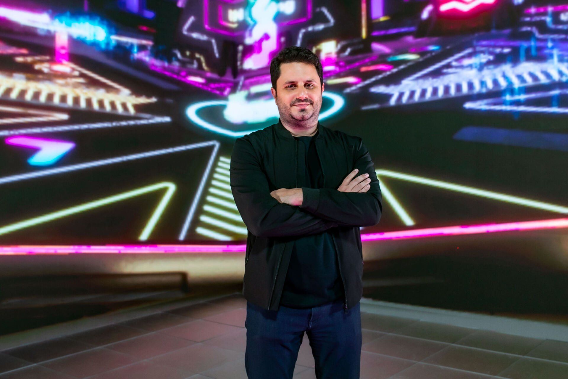 Um homem está de pé em frente a uma tela grande com os braços cruzados.