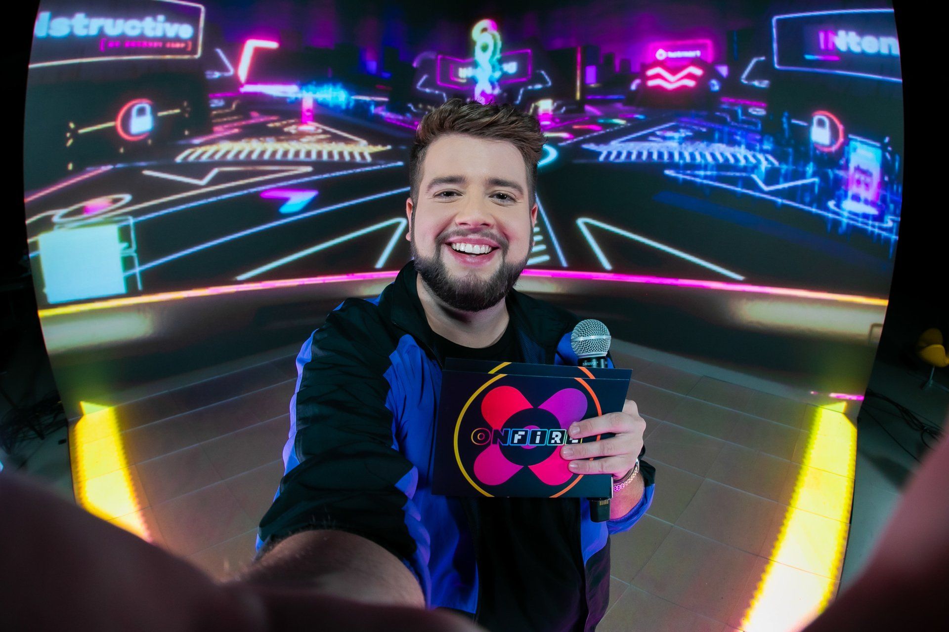 Um homem está tirando uma selfie em frente a uma tela enquanto segura um microfone.