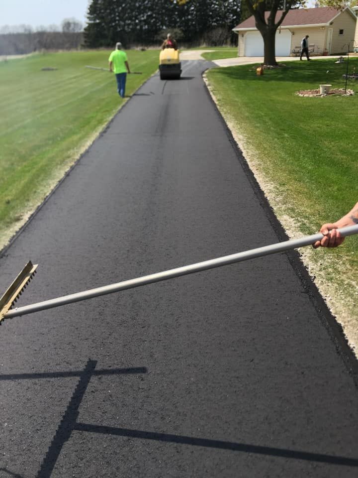 A person is holding a rake on the side of a road.
