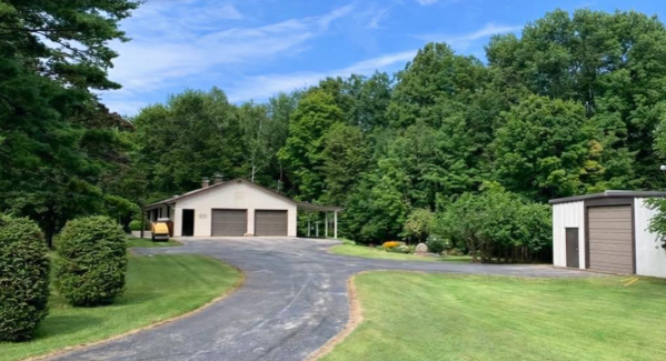 Driveway leading to a house with a two-car garage, surrounded by green grass and trees under a blue sky.