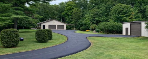 Driveway leading to a house with a two-car garage, surrounded by green grass and trees under a blue sky.