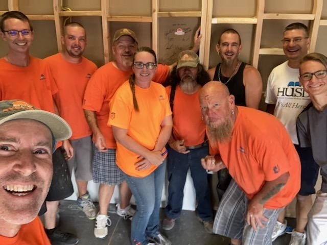 Group of people in orange shirts, smiling for a photo indoors, likely during construction.