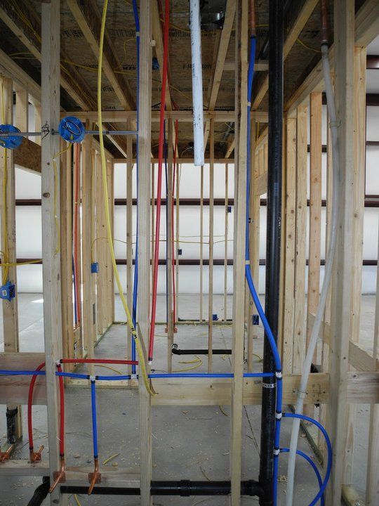Wooden frame construction with plumbing and electrical wiring. Blue, red, and yellow pipes and wires visible.