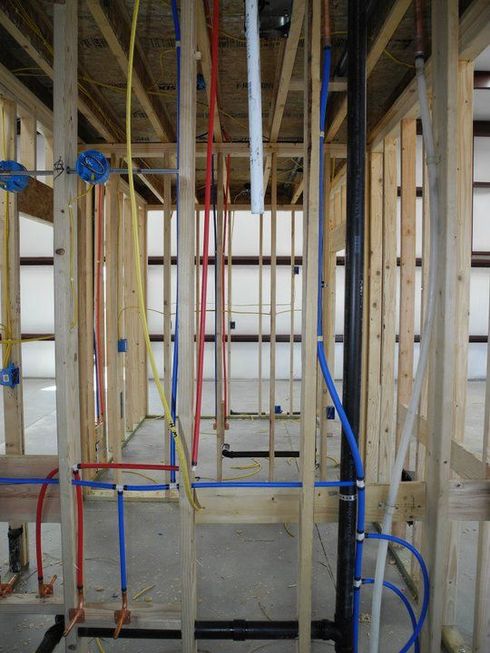 Wooden frame construction with plumbing and electrical wiring. Blue, red, and yellow pipes and wires visible.