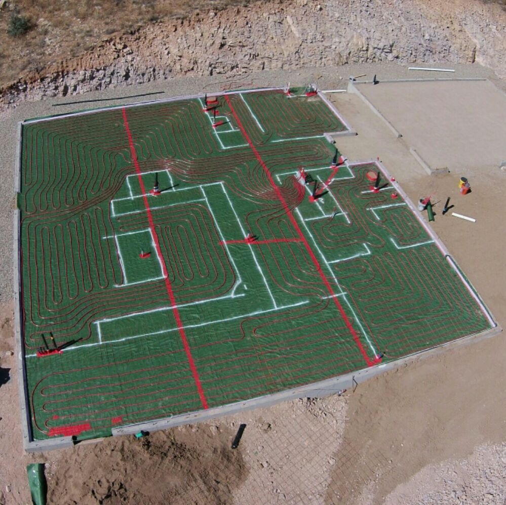 Aerial view of a construction site with green, grid-like pattern showing foundation layout, red lines, white markings, and workers.