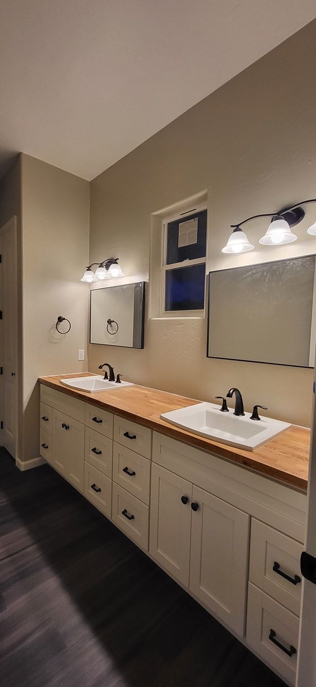Bathroom with white cabinets, wood countertop, two sinks, and mirrors.