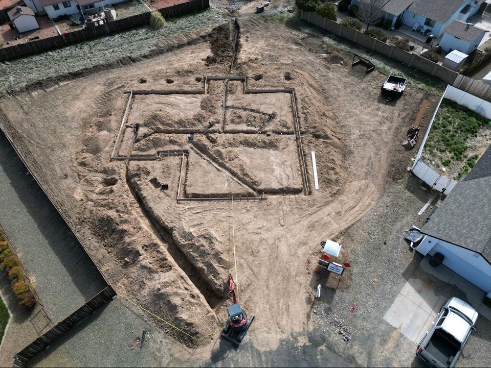 Aerial view of a construction site with foundation trenches and an excavator.