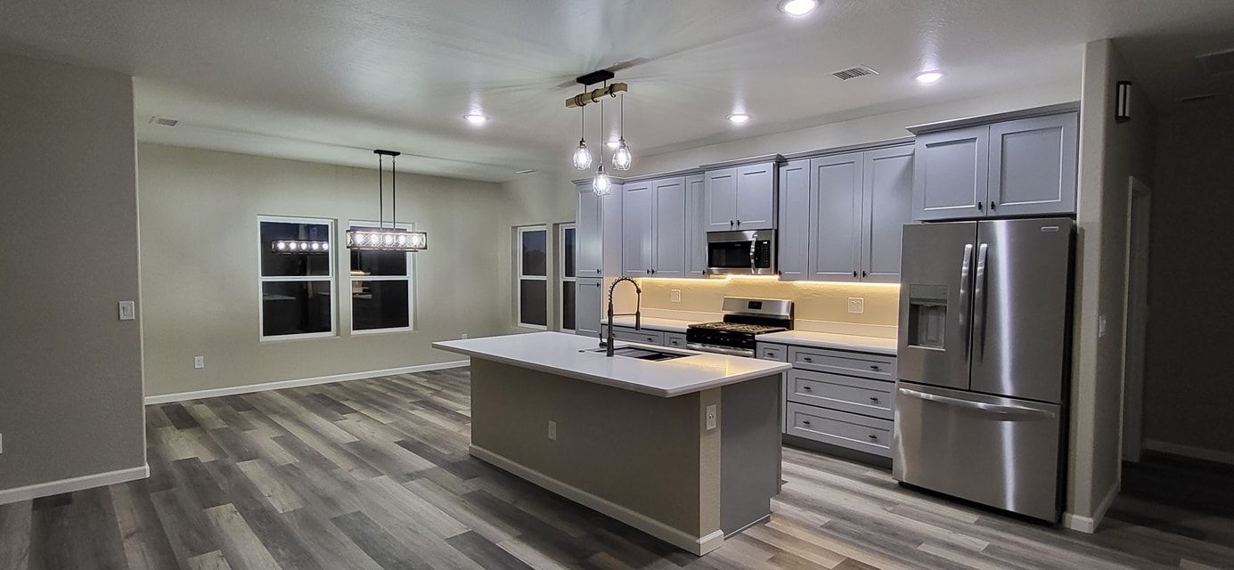 Kitchen with island, stainless steel appliances, and gray cabinets. Light wood-look flooring.
