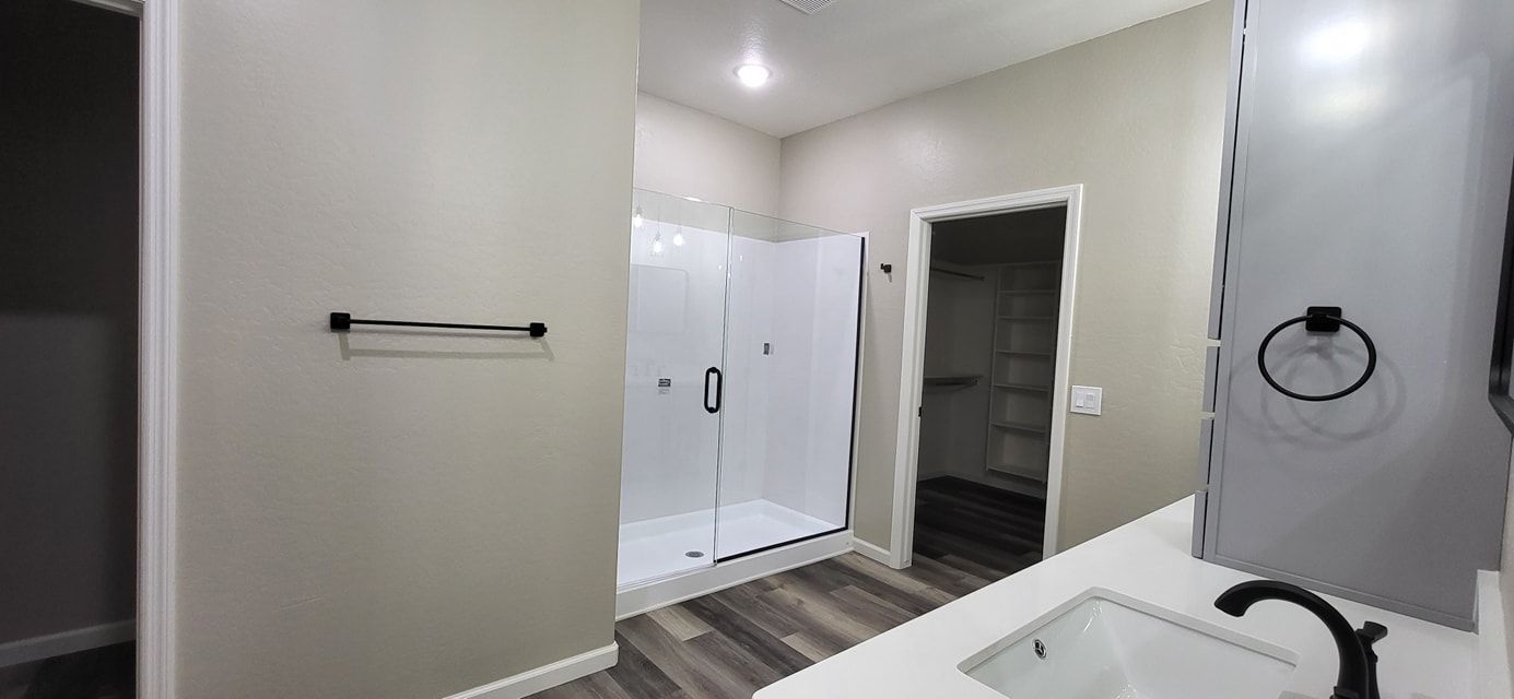 Bathroom with a white shower, a vanity, and a walk-in closet. The walls are gray, and the floor is wood-like.