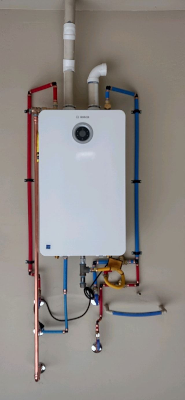 A wall-mounted, white gas-powered water heater with red, blue, and copper pipes.