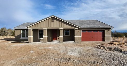 Tan stucco house with red garage door, sitting in a dirt lot under a blue sky.