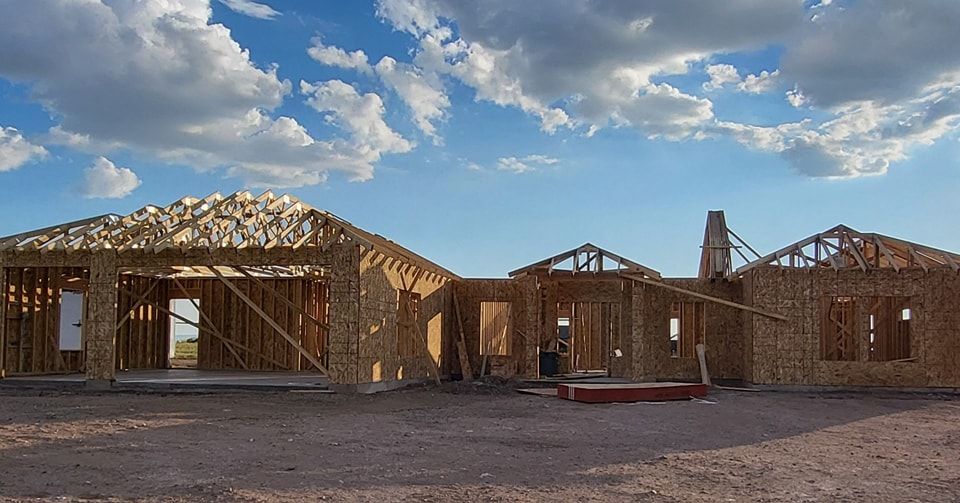 House under construction, wooden frame, blue sky with clouds.