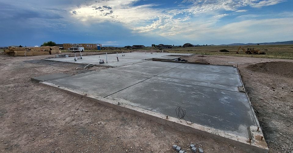Newly poured concrete foundation on a dry, dirt lot, with a cloudy sky in the background.