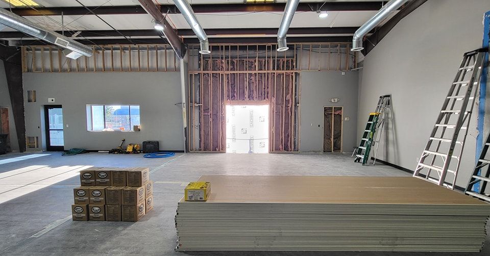 Interior construction site; empty room with exposed framing, drywall, and equipment.