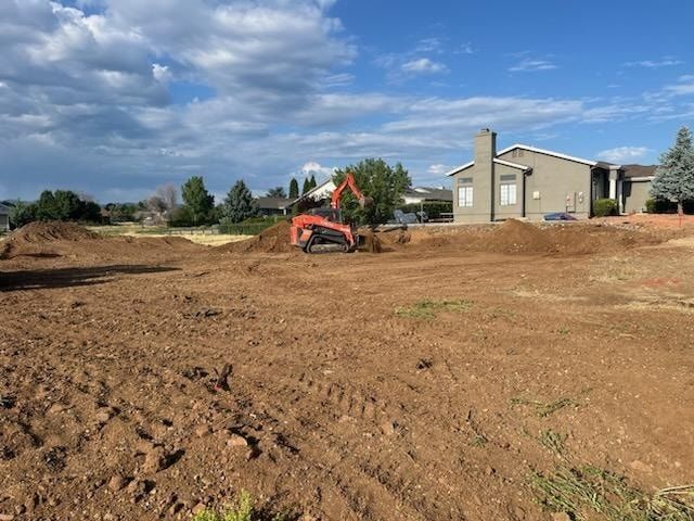 An excavator on a dirt lot next to a house under a partly cloudy sky.