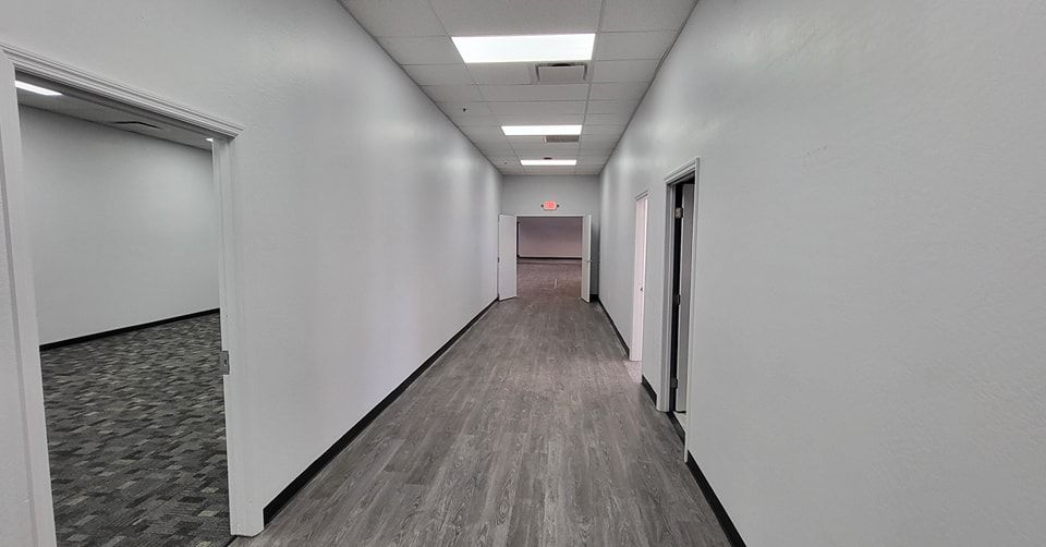 Long, white-walled office hallway with a dark floor, doors, and overhead lights.